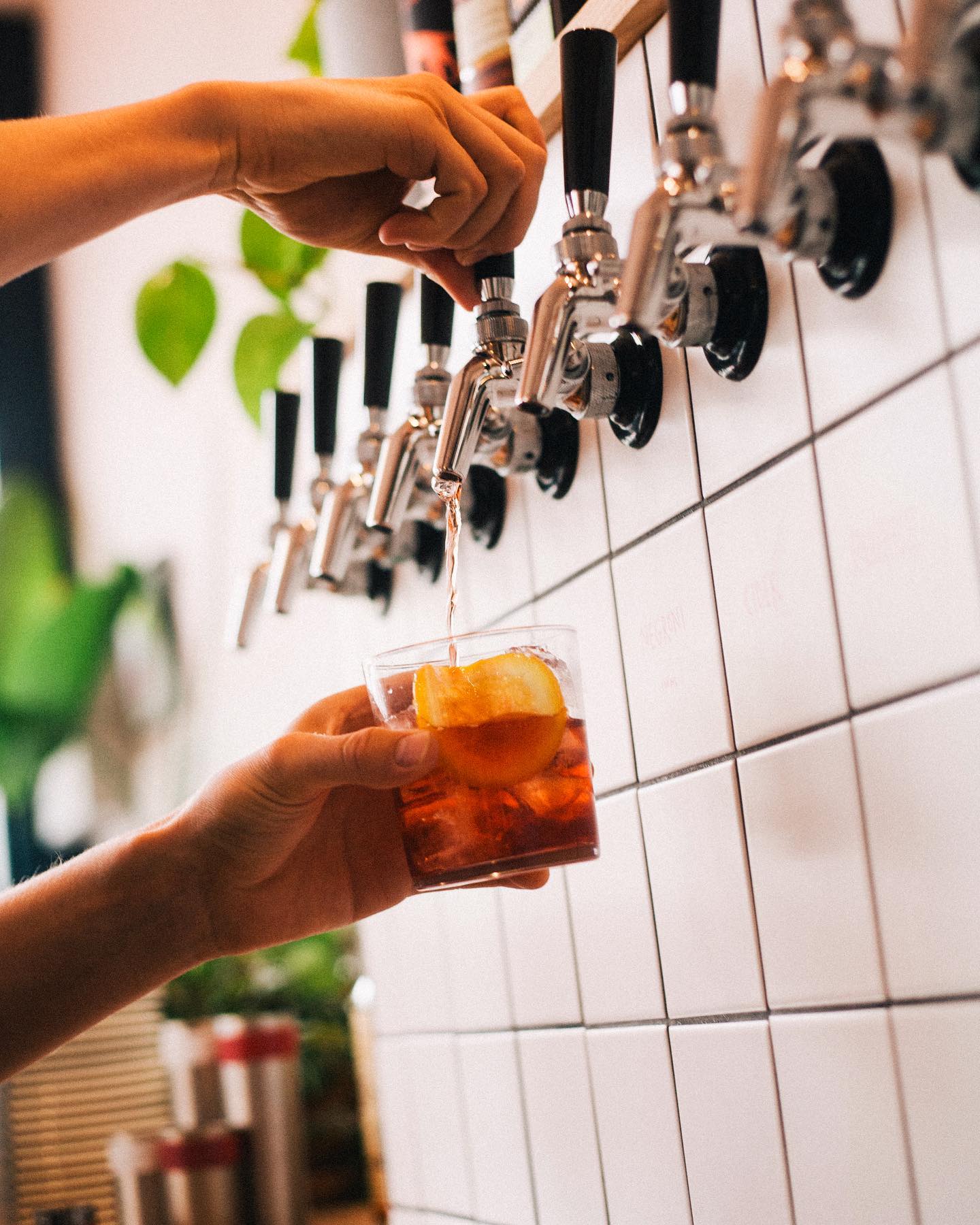 A bartender pours craft beer from chrome taps into a glass held by a customer at a modern brewery or pub.