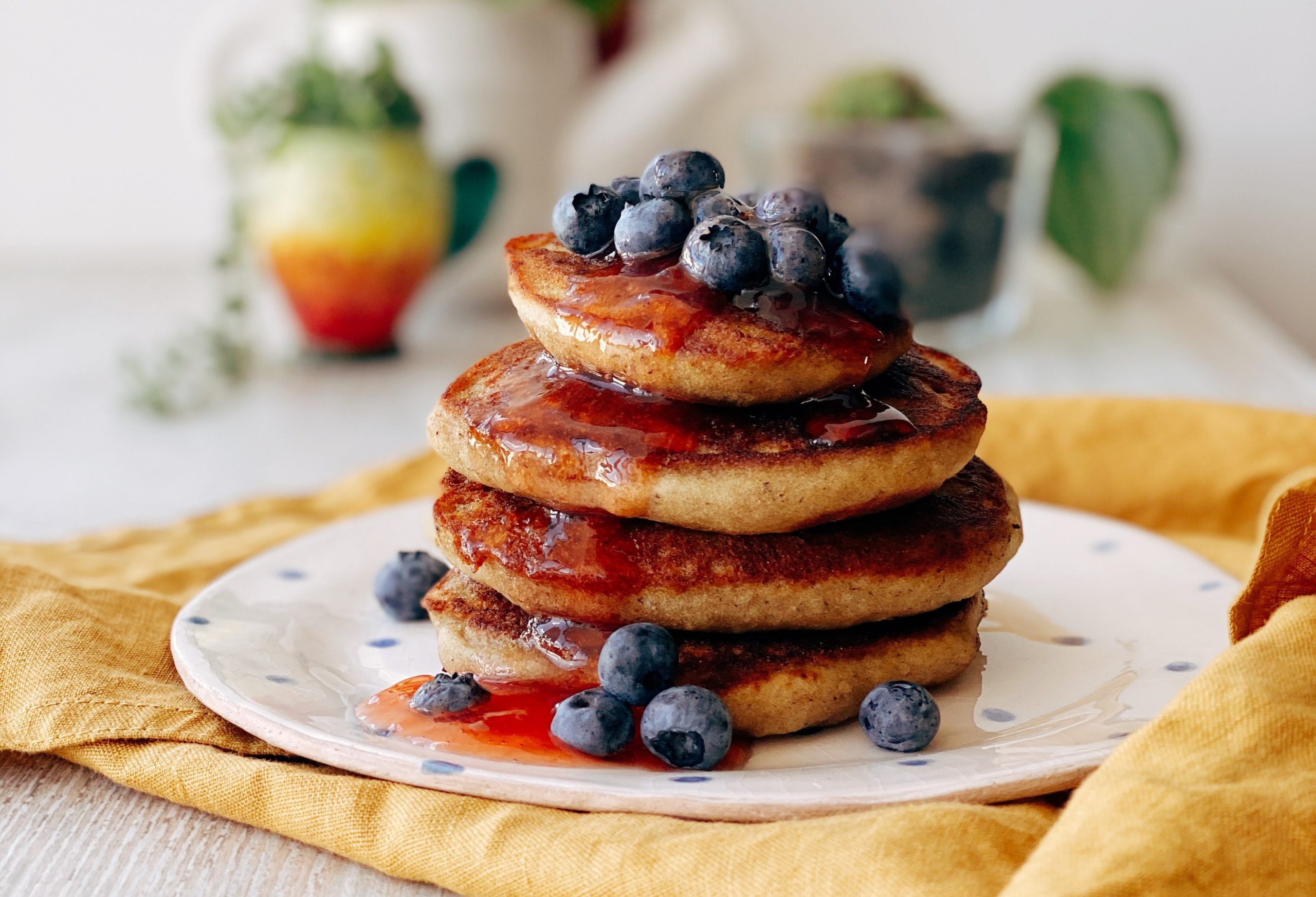 A stack of golden pancakes topped with fresh blueberries and syrup on a white polka-dot plate.