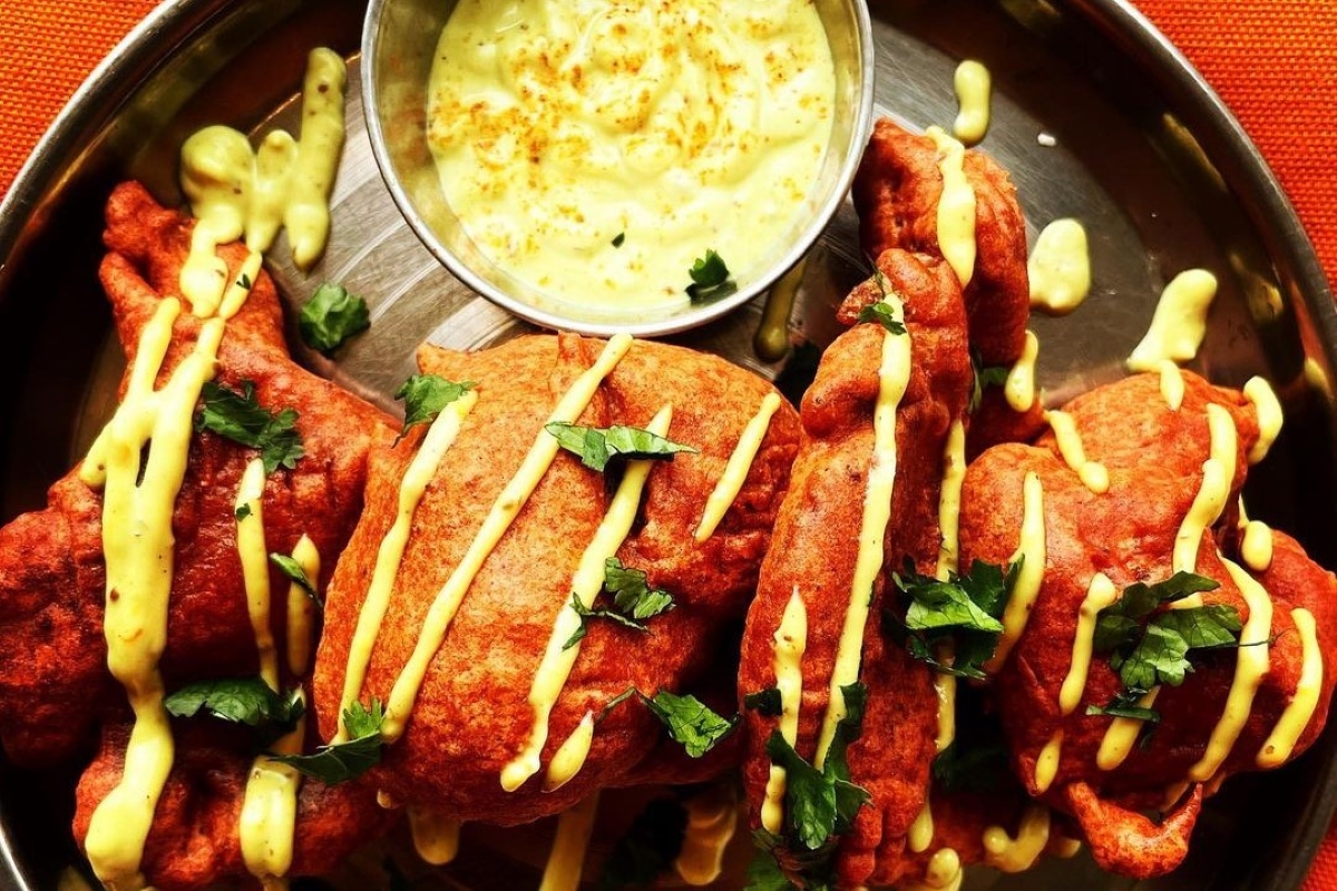 Grilled lobster tails with yellow sauce drizzle and herbs, served on a metal platter with dipping sauce.