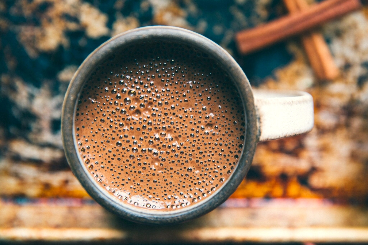 A ceramic mug filled with frothy hot chocolate topped with small bubbles, sitting on a wooden surface.