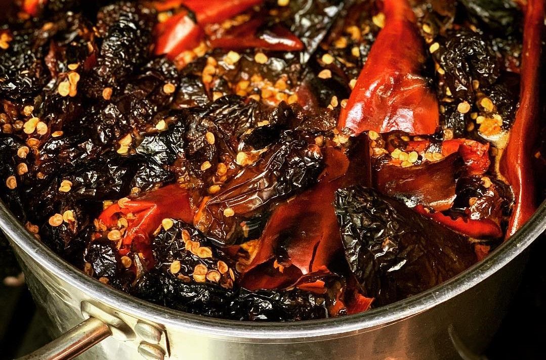 Dark dried chiles and red peppers with spices simmering in a metal pot, ingredients for traditional Mexican mole sauce.