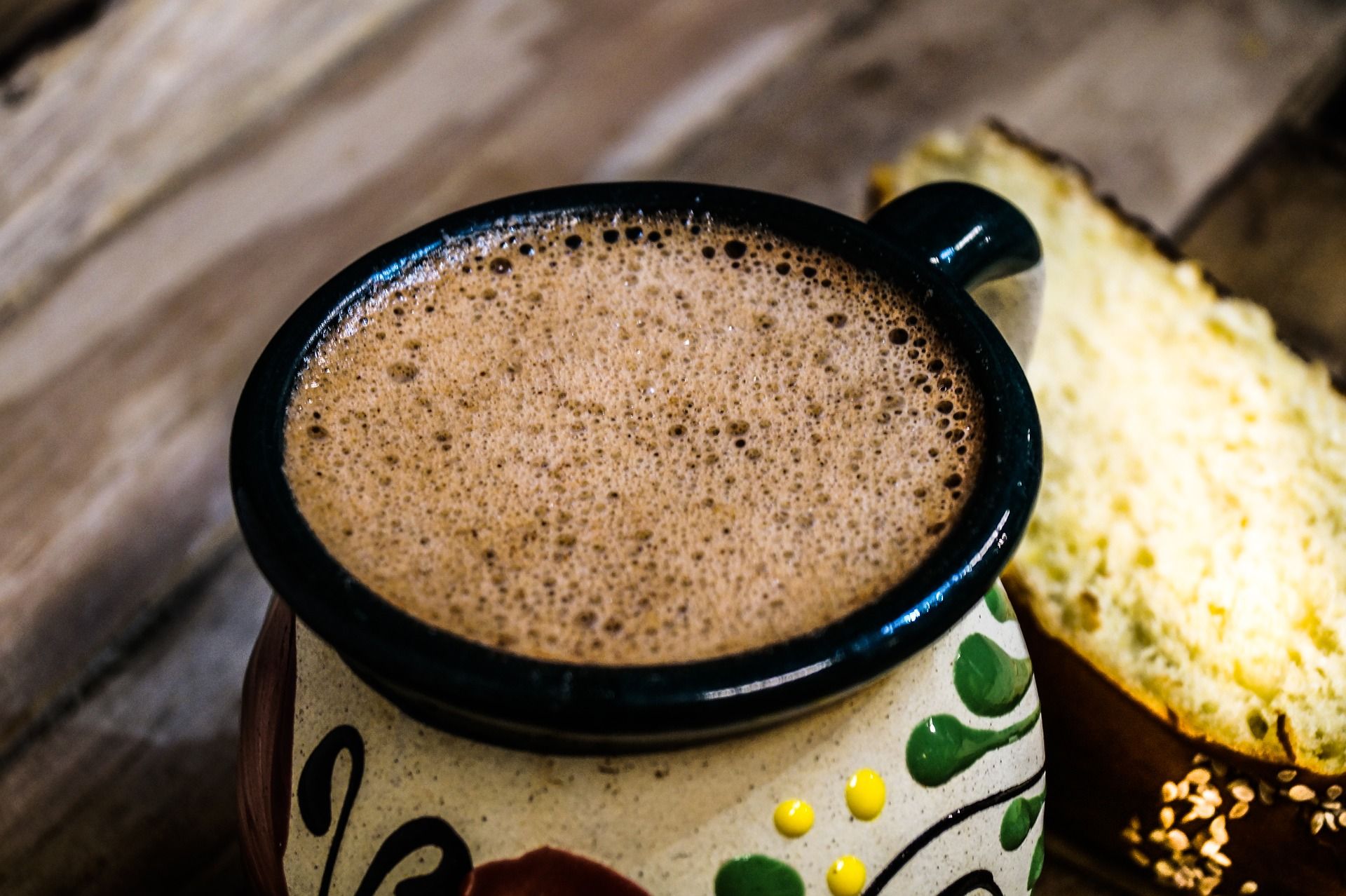 A frothy cup of Mexican hot chocolate with traditional foam sits next to tortillas on a wooden surface.