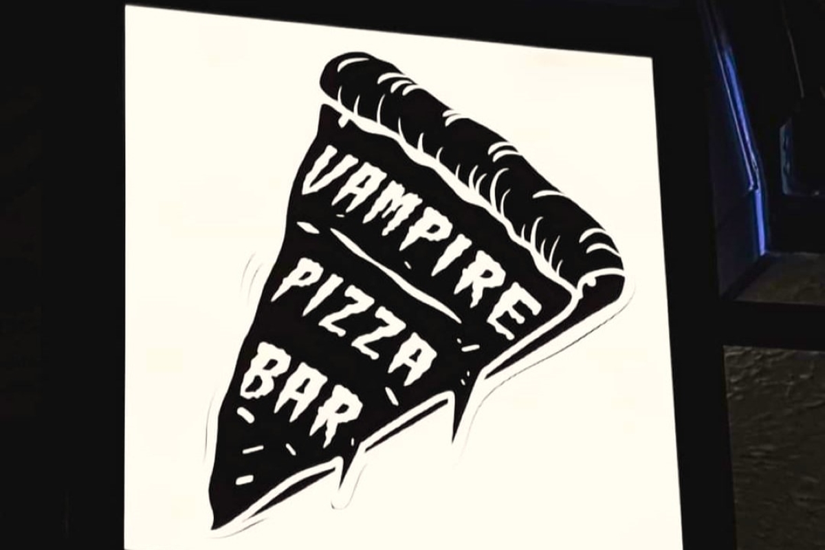 Black and white artistic illustration of a pizza slice with "VAMPIRE PIZZA BAR" text inside on a white poster.