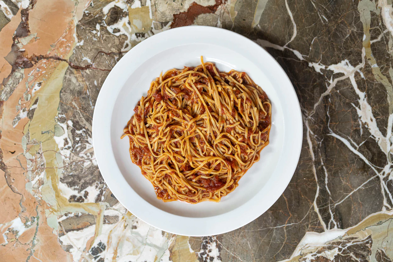 A plate of spaghetti with rich tomato sauce on a marble surface, photographed from above.