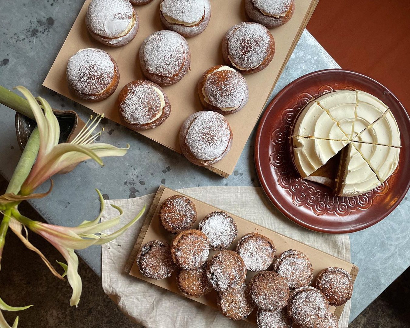 Powdered sugar-dusted pastries arranged on wooden boards alongside sliced white cake on a decorative brown plate.