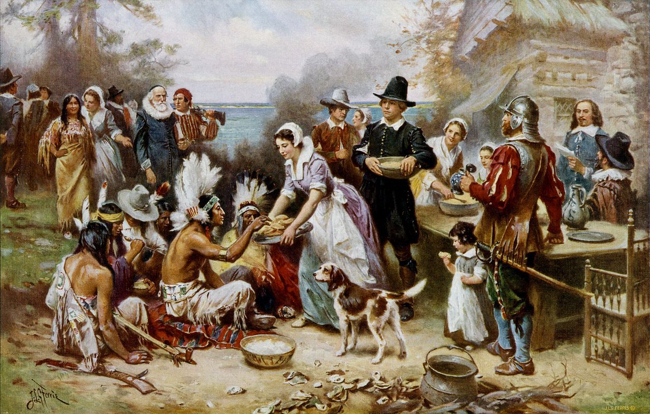 A romanticized painting depicting Pilgrims and Native Americans sharing a feast outdoors, with bowls of food and harvest goods scattered around the gathering.