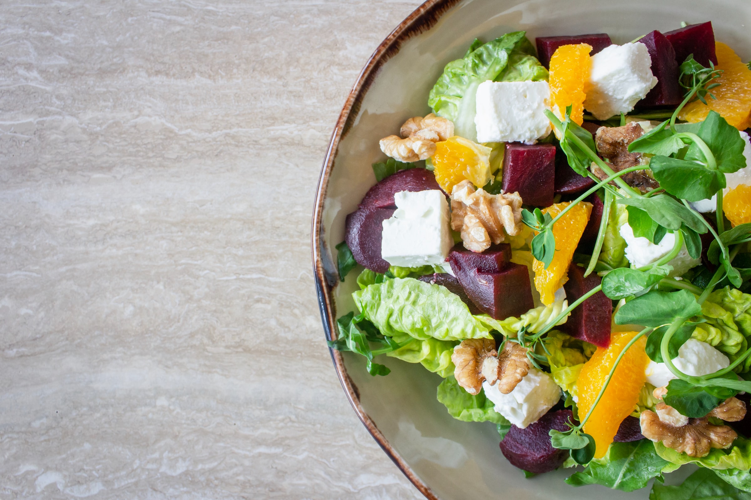 A colorful salad with roasted beets, orange segments, walnuts, goat cheese, and mixed greens in a ceramic bowl.