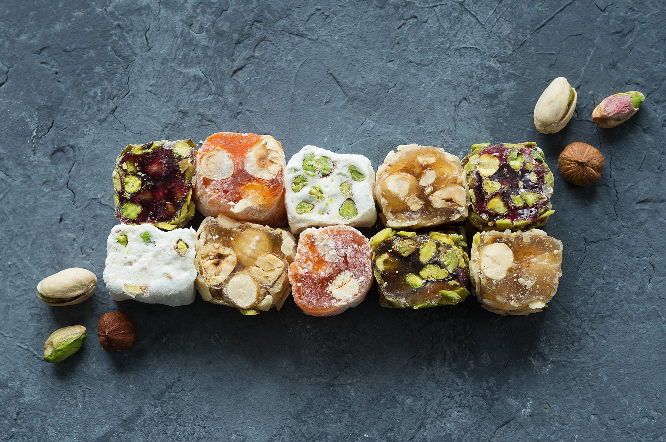 Colorful Turkish delight and lokum sweets with pistachios and nuts arranged on dark slate surface.