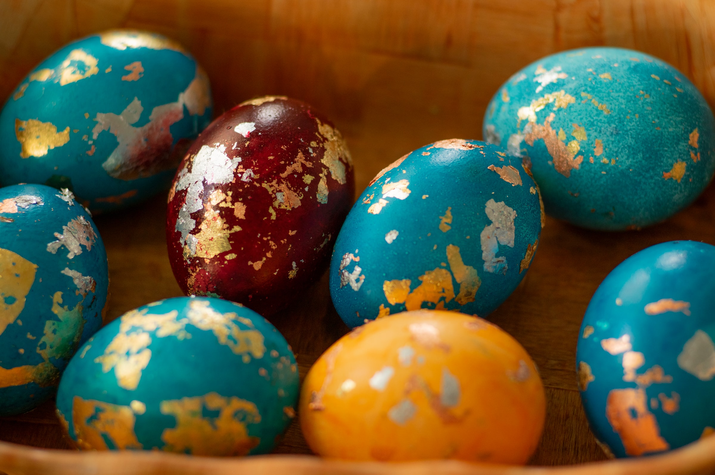 Colorful decorated Easter eggs with peeling paint in blue, red, and orange sit in a wooden bowl.