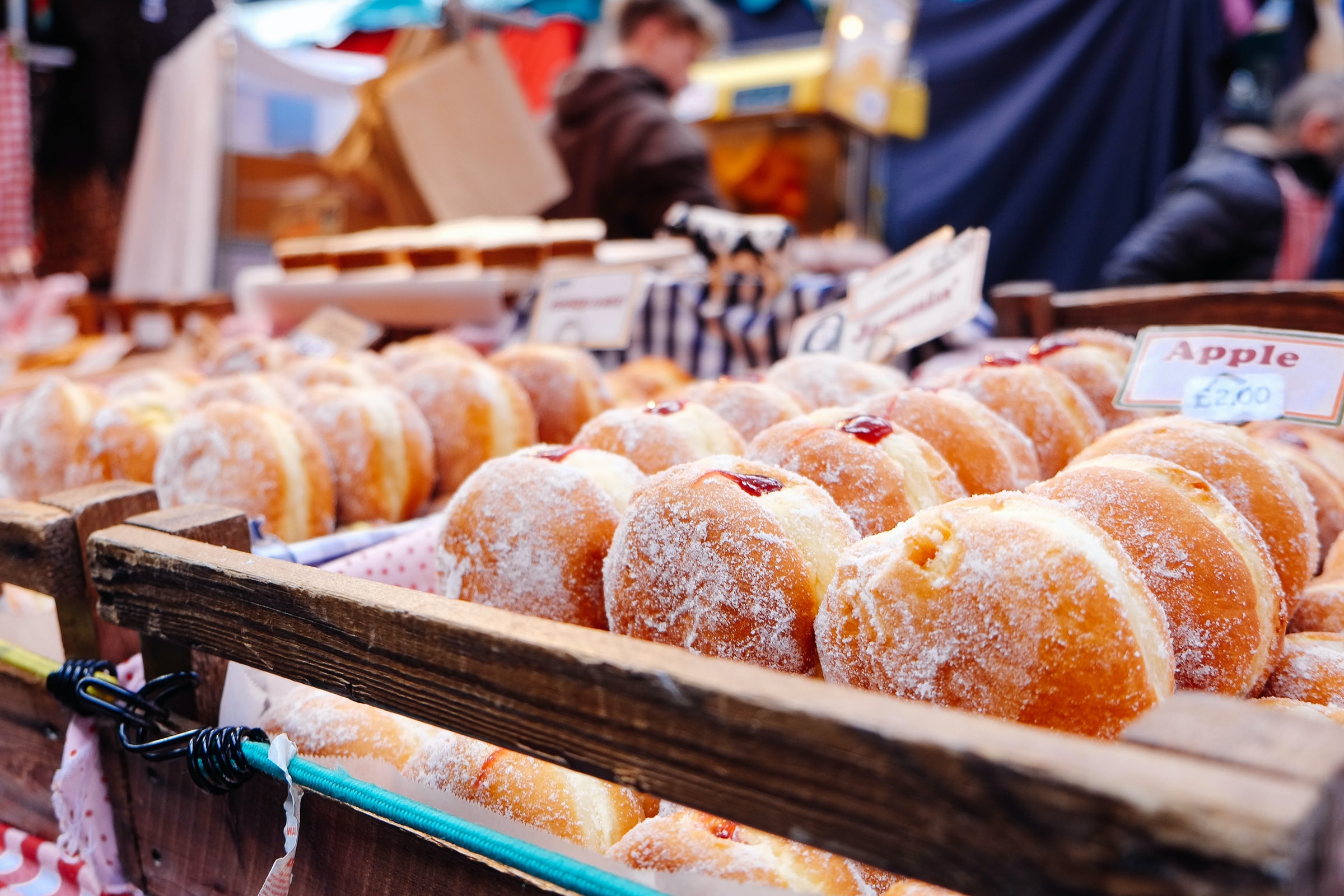 Fresh jelly-filled donuts dusted with powdered sugar displayed in wooden crates at a market stall.