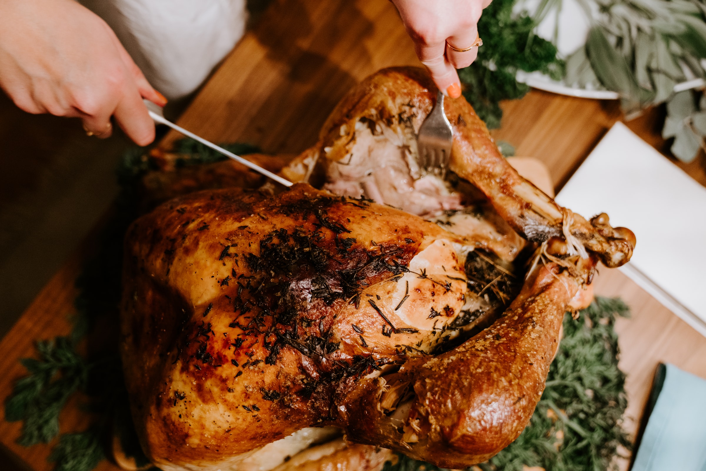 Hands carving a golden-brown roasted turkey with a carving knife and fork on a wooden cutting board.