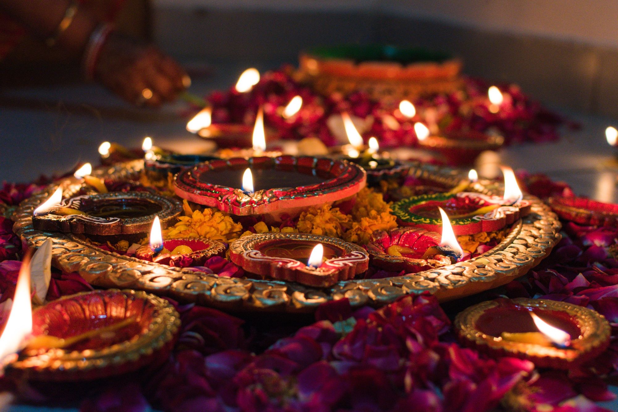 Ornate oil lamps and diyas with flickering flames arranged on decorative plates, surrounded by marigold flowers and rose petals for Diwali.