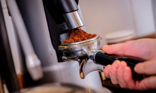 A professional espresso machine brewing coffee with ground coffee beans visible in the portafilter basket.