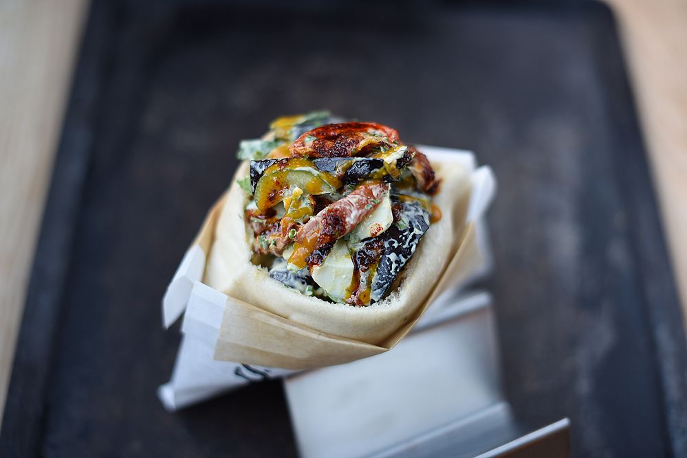 A soft pita sandwich filled with roasted vegetables including eggplant and peppers, wrapped in parchment paper on a dark slate.