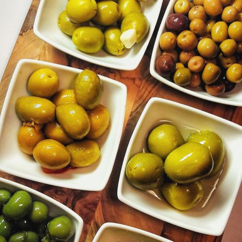 Various marinated olives in different colors and sizes displayed in white ceramic bowls on a wooden surface.