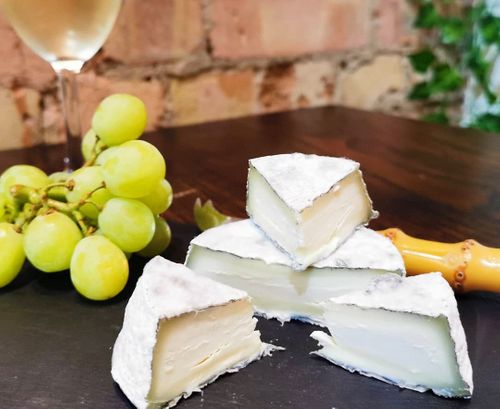 Wedges of soft white cheese with creamy interior on a slate board alongside green grapes and a glass of white wine.