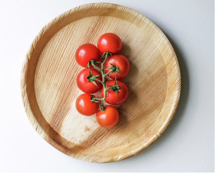 Fresh cherry tomatoes on the vine arranged on a wooden plate, showcasing sustainable eco-friendly dishware.